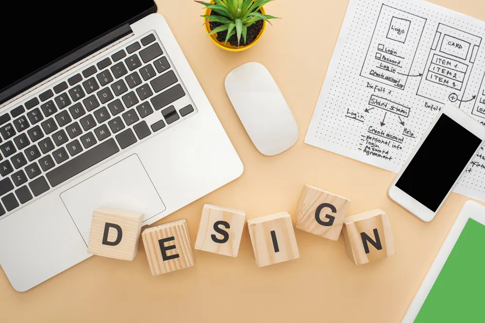 Riječ design složena drvenim kockama uz laptop i wireframe skicu