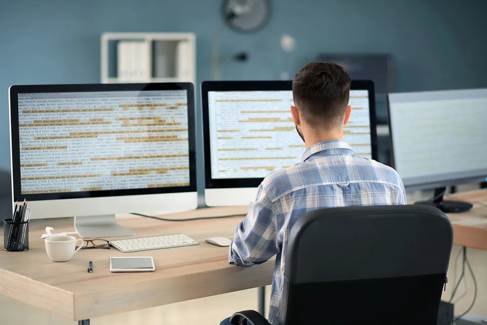 Web developer pregledava kod web stranice na tri monitora