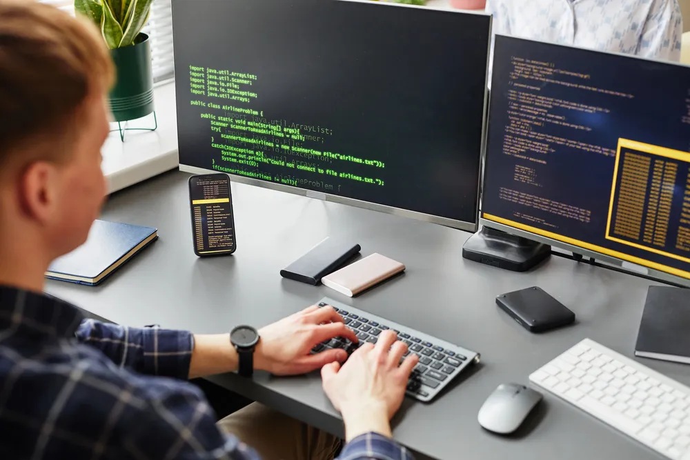 Programer piše programski kod na dva ekrana u uredu
