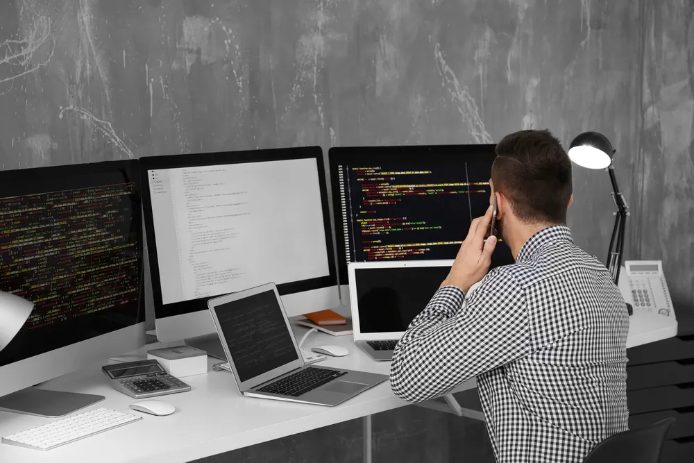 Programer za radnom stanicom s više monitora punih koda
